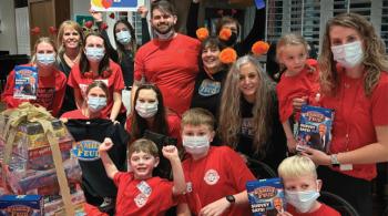 A group of children and adults pose for a photo at Ronald McDonald House. Most of them are wearing red t-shirts.